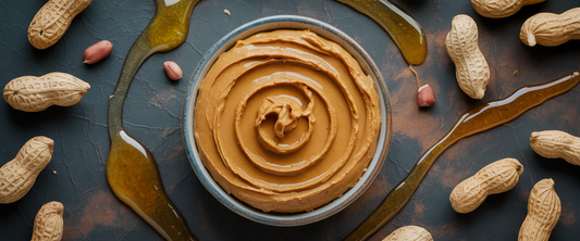 Artisanal peanut butter in a ceramic dish with a honey drizzle on dark slate, surrounded by whole peanuts; rich shadows and macro detail.